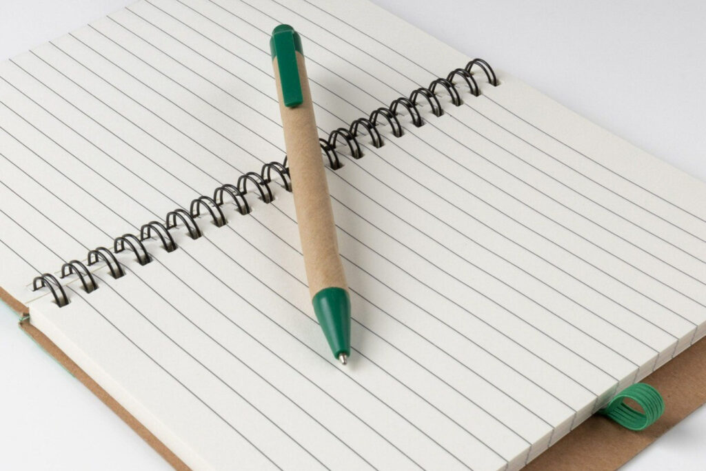 A ballpoint pen lying across an open notepad with blank pages